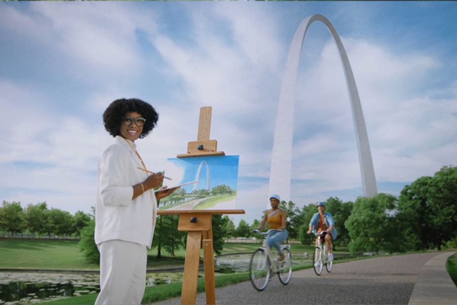 A woman paints a picture of the St. Louis Arch with the Arch visible in the background.